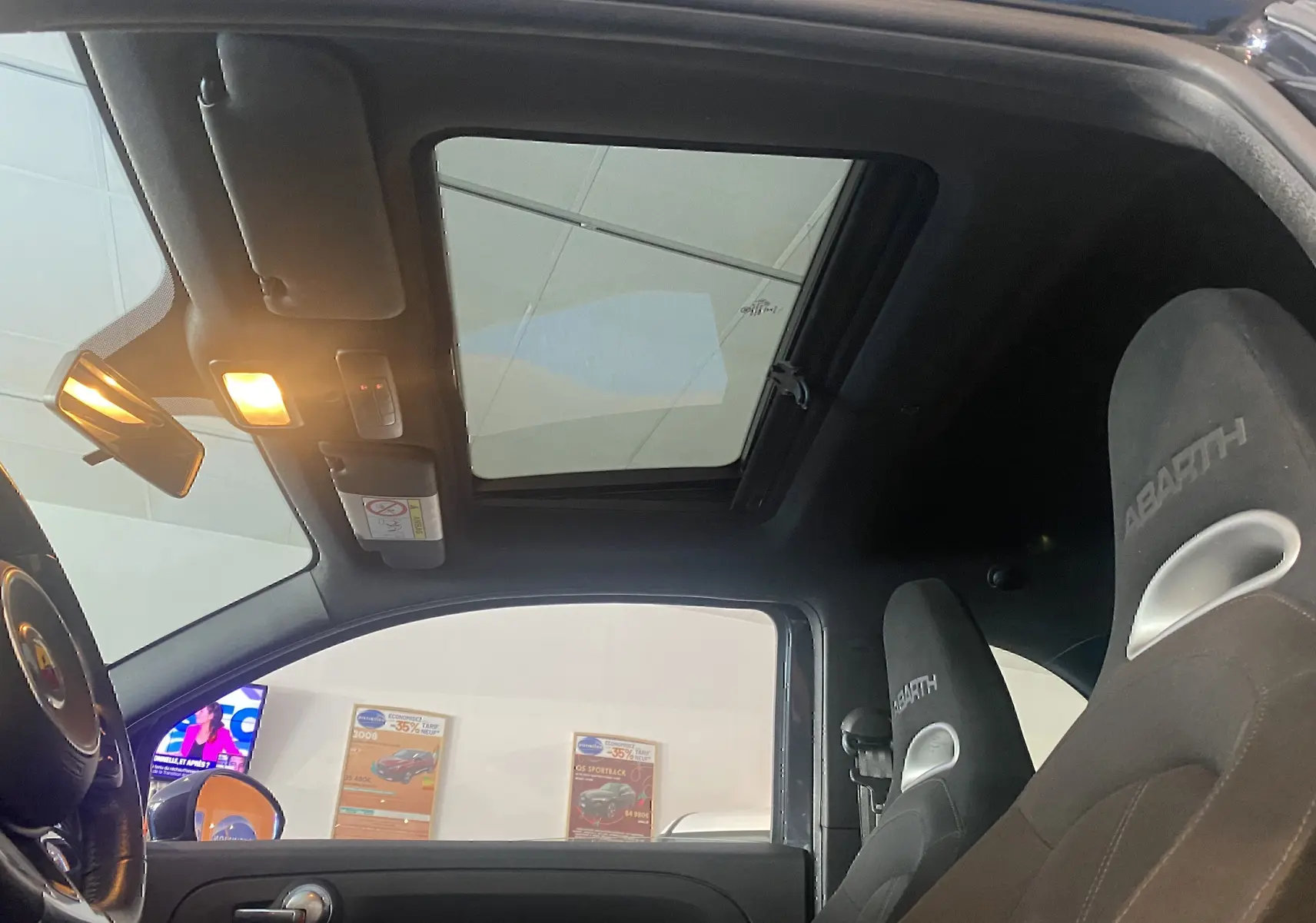 Intérieur noir d'une Abarth 595 2018 avec toit ouvrant électrique et sièges sport marqués Abarth vus côté gauche.