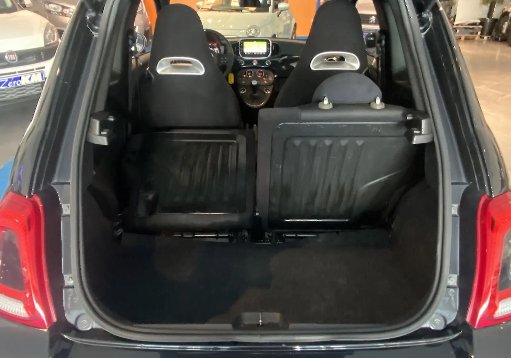 Vue arrière du coffre ouvert de l'Abarth 595 noire, montrant les sièges avant et l'écran GPS intérieur.