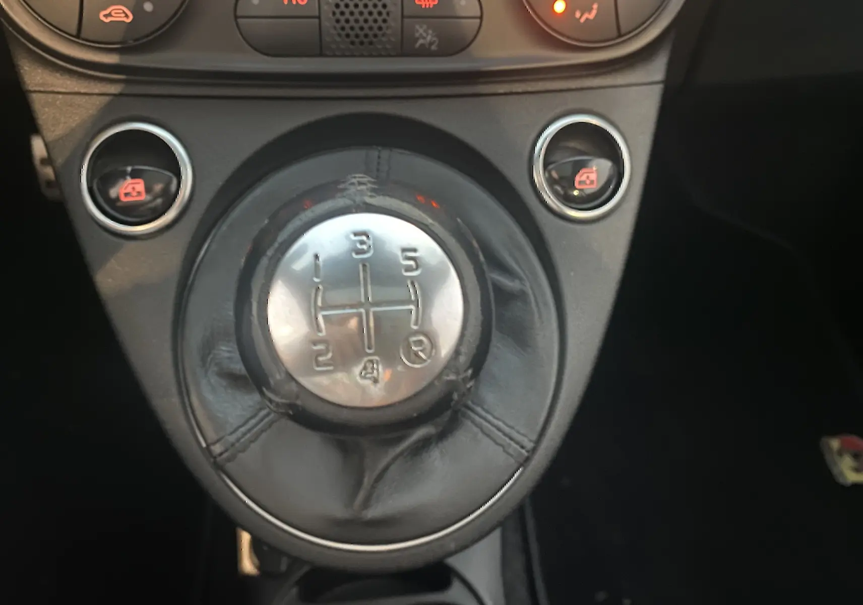 Gros plan sur le levier de vitesses manuel noir de l'Abarth 595 2018 avec boutons de commande et console sombre.