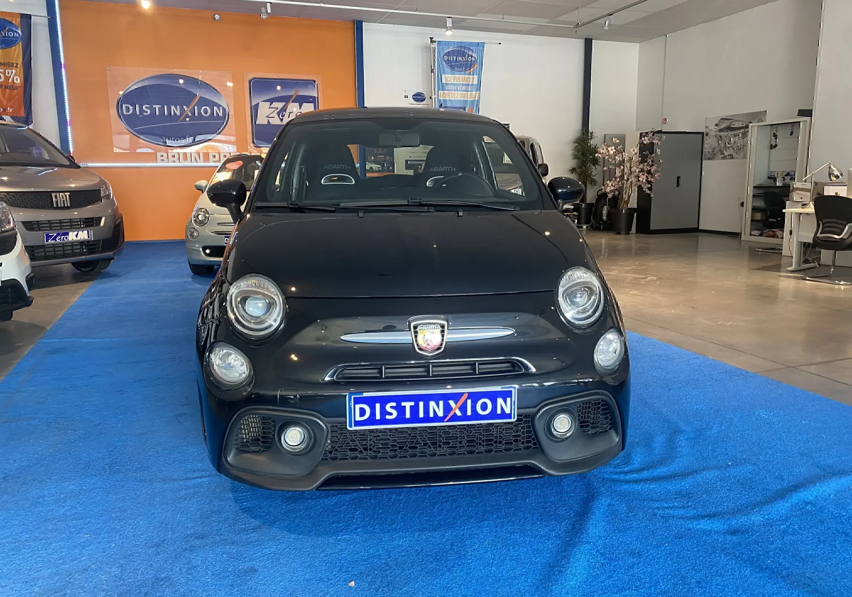 Vue frontale de l'Abarth 595 noire 2018 avec logo Abarth visible et sièges sport en intérieur showroom.