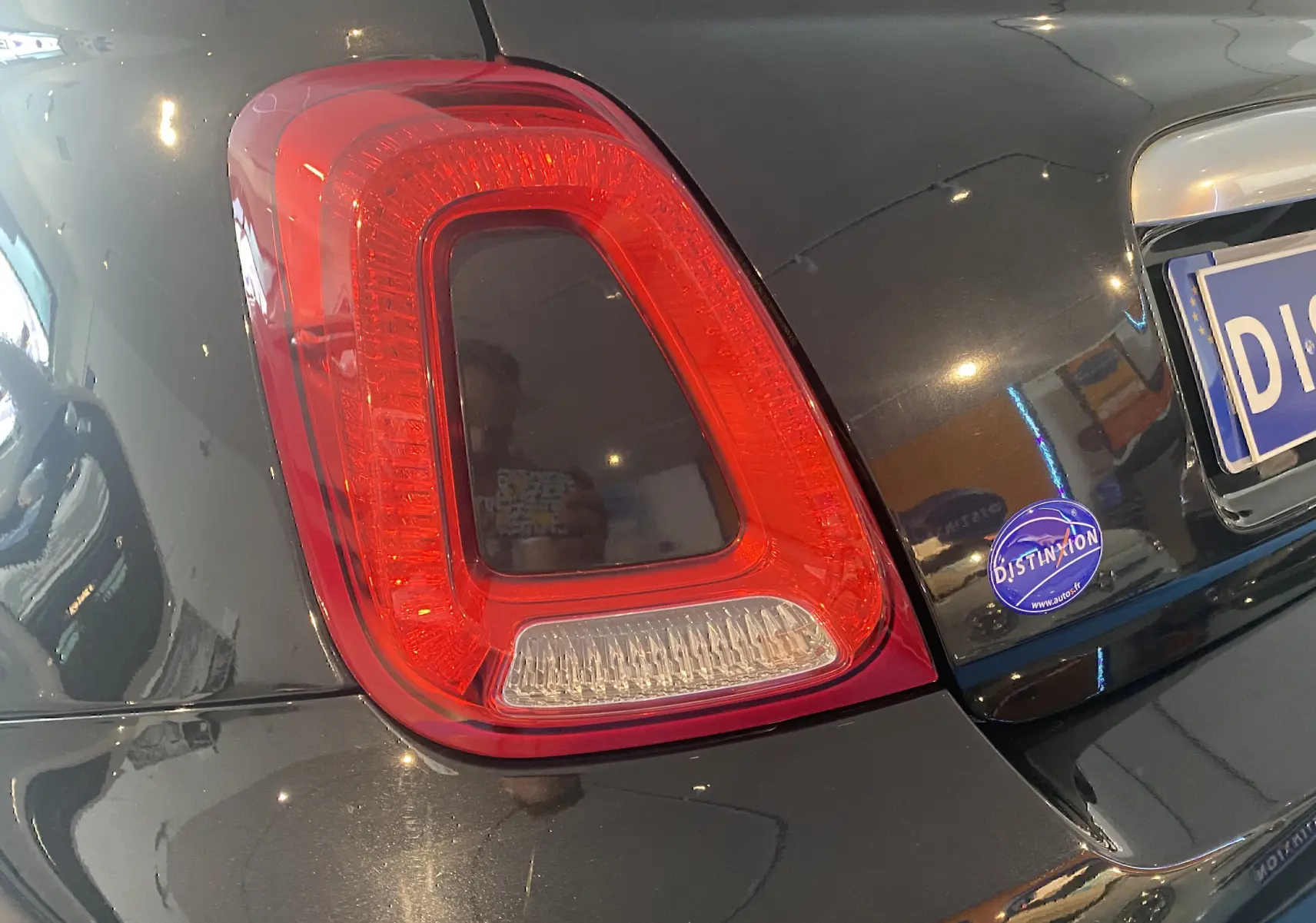 Gros plan sur le feu arrière gauche d'une ABARTH 595 noire, avec reflet intérieur et autocollant Distinxion sur le coffre.