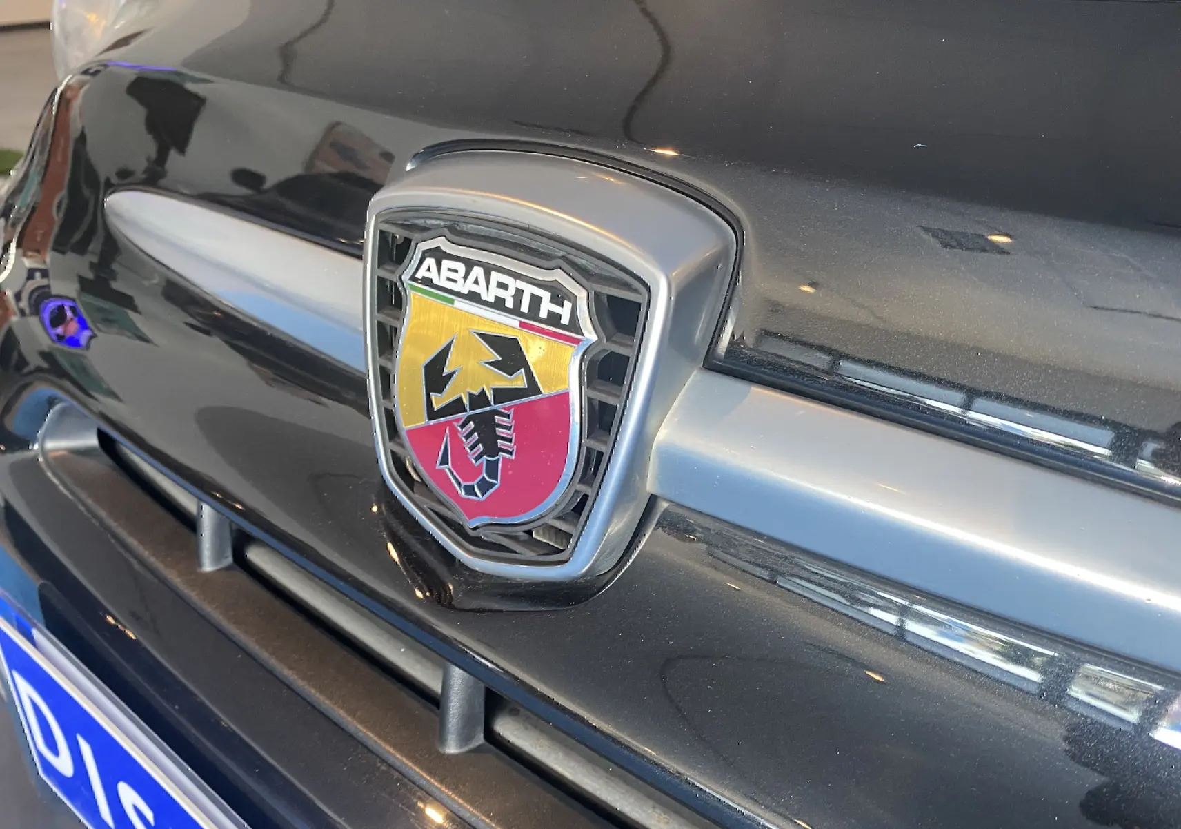 Gros plan sur l'emblème ABARTH noir et rouge sur la calandre avant noire de l'Abarth 595.