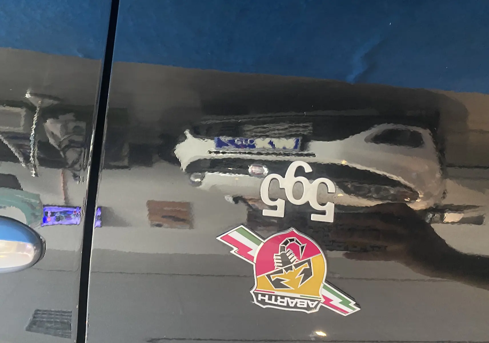 Gros plan sur la porte noire d'une Abarth 595 avec logo scorpion et badge 595 blanc visible en reflet.