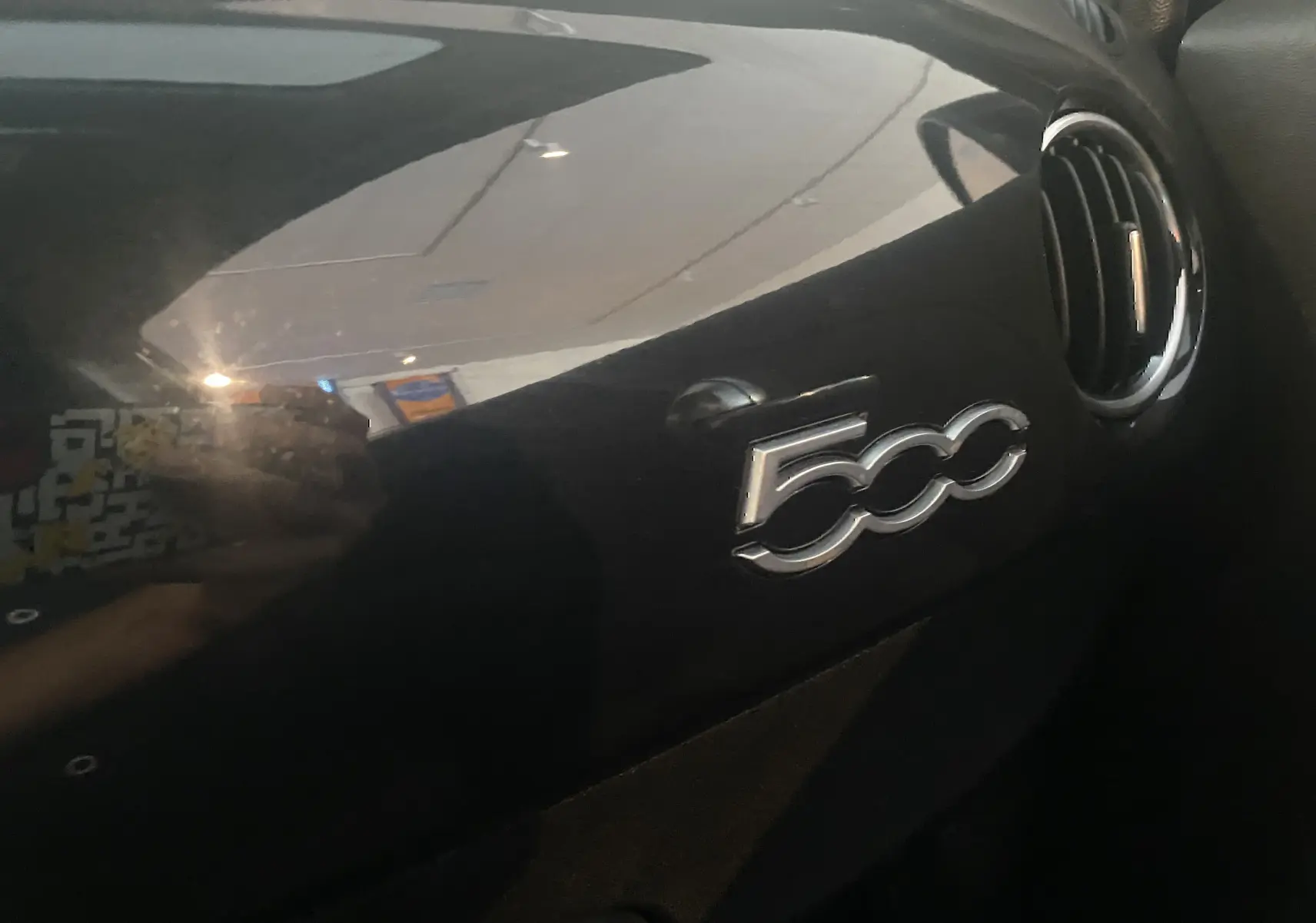 Gros plan sur le tableau de bord noir brillant avec logo 500 et une sortie d'air ronde à droite dans un Abarth 595 2018.