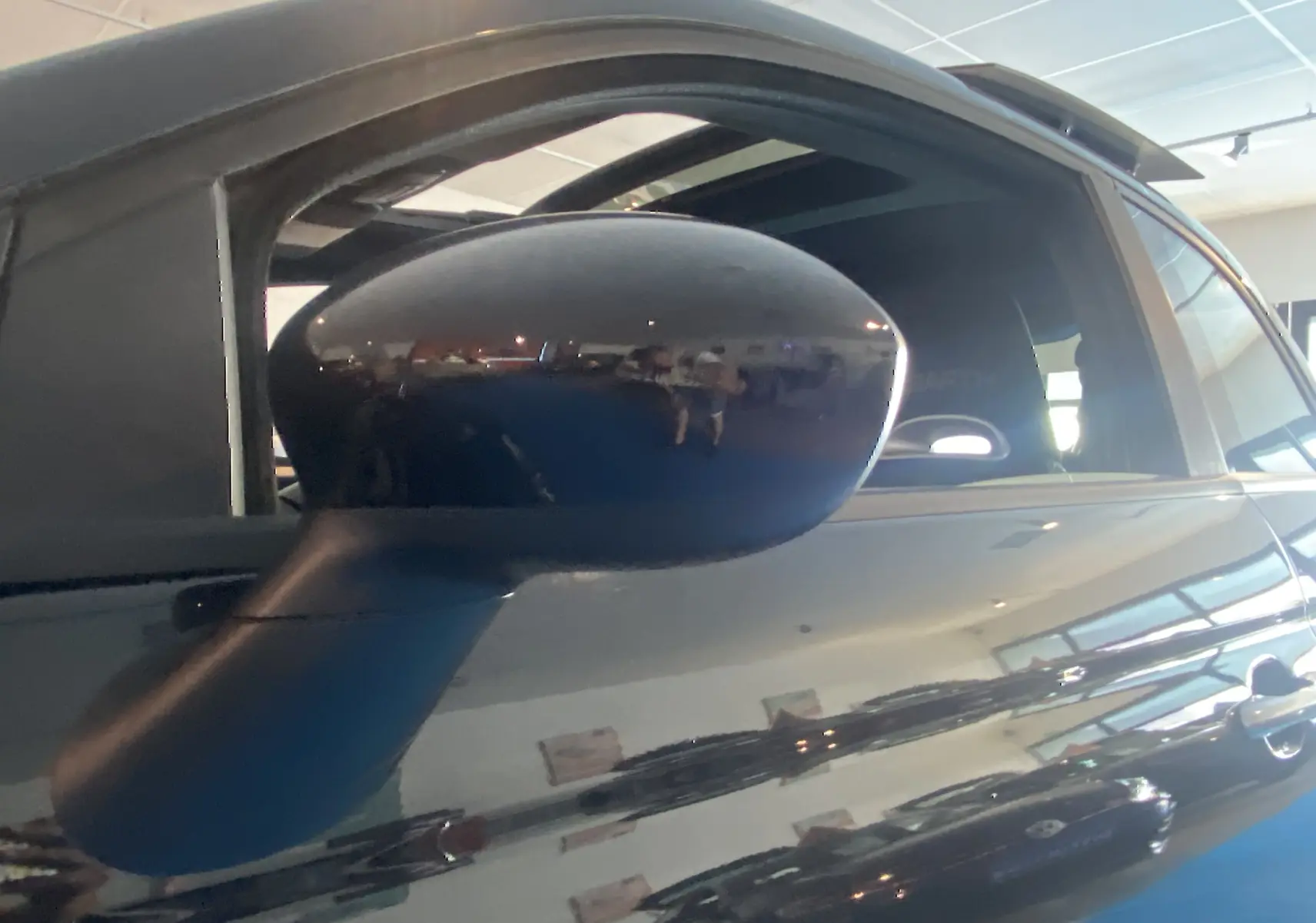 Rétroviseur côté gauche noir brillant d'une ABARTH 595 noire avec toit ouvrant électrique visible en intérieur showroom.