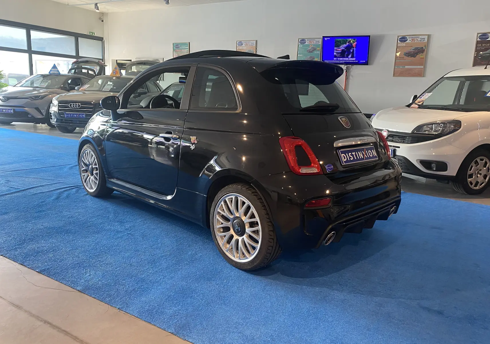 Vue 3/4 arrière droite d'une ABARTH 595 noire avec jantes alu 17 pouces et toit ouvrant dans un showroom.