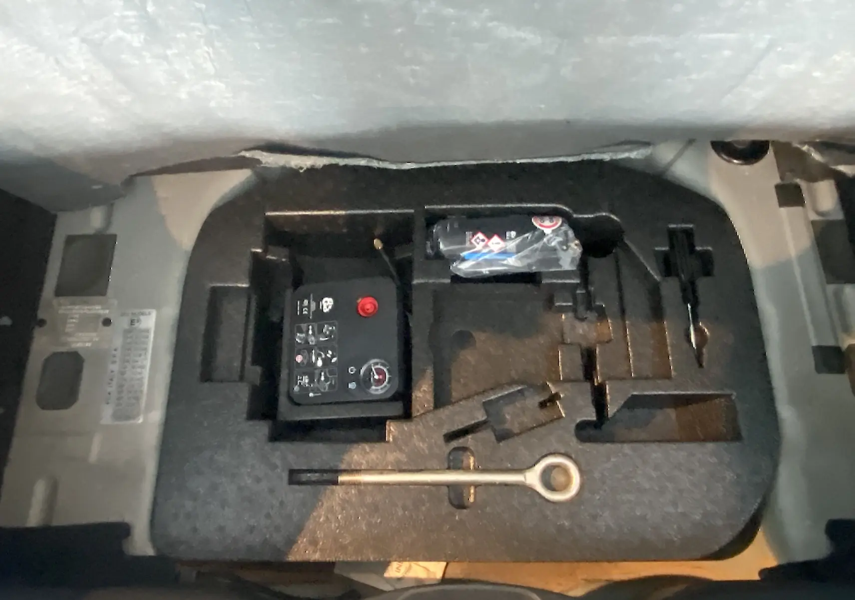 Gros plan sur le coffre d’un Abarth 595 noir de 2018 montrant le kit de réparation et les outils de bord.