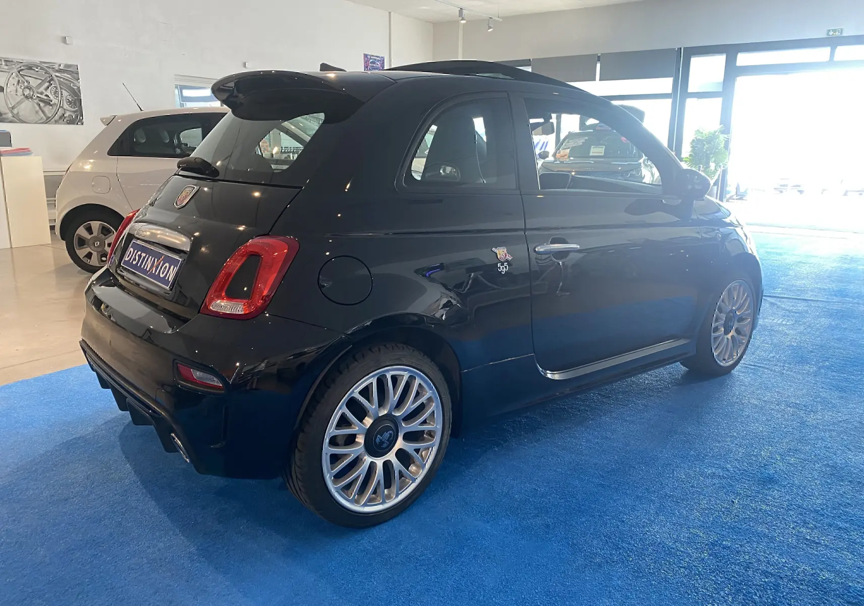 Vue 3/4 arrière droite d'une ABARTH 595 noire avec jantes alu 17 pouces et toit ouvrant électrique en intérieur showroom.