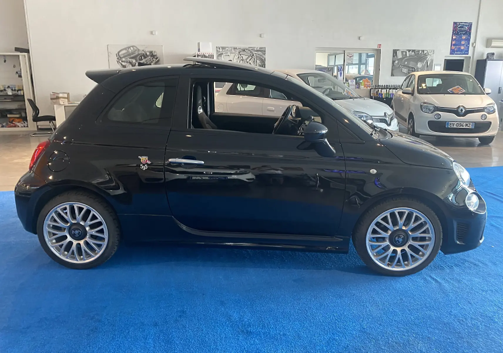 Profil droit d'une ABARTH 595 noire 2018 avec jantes alu 17 pouces et toit ouvrant électrique en intérieur showroom.