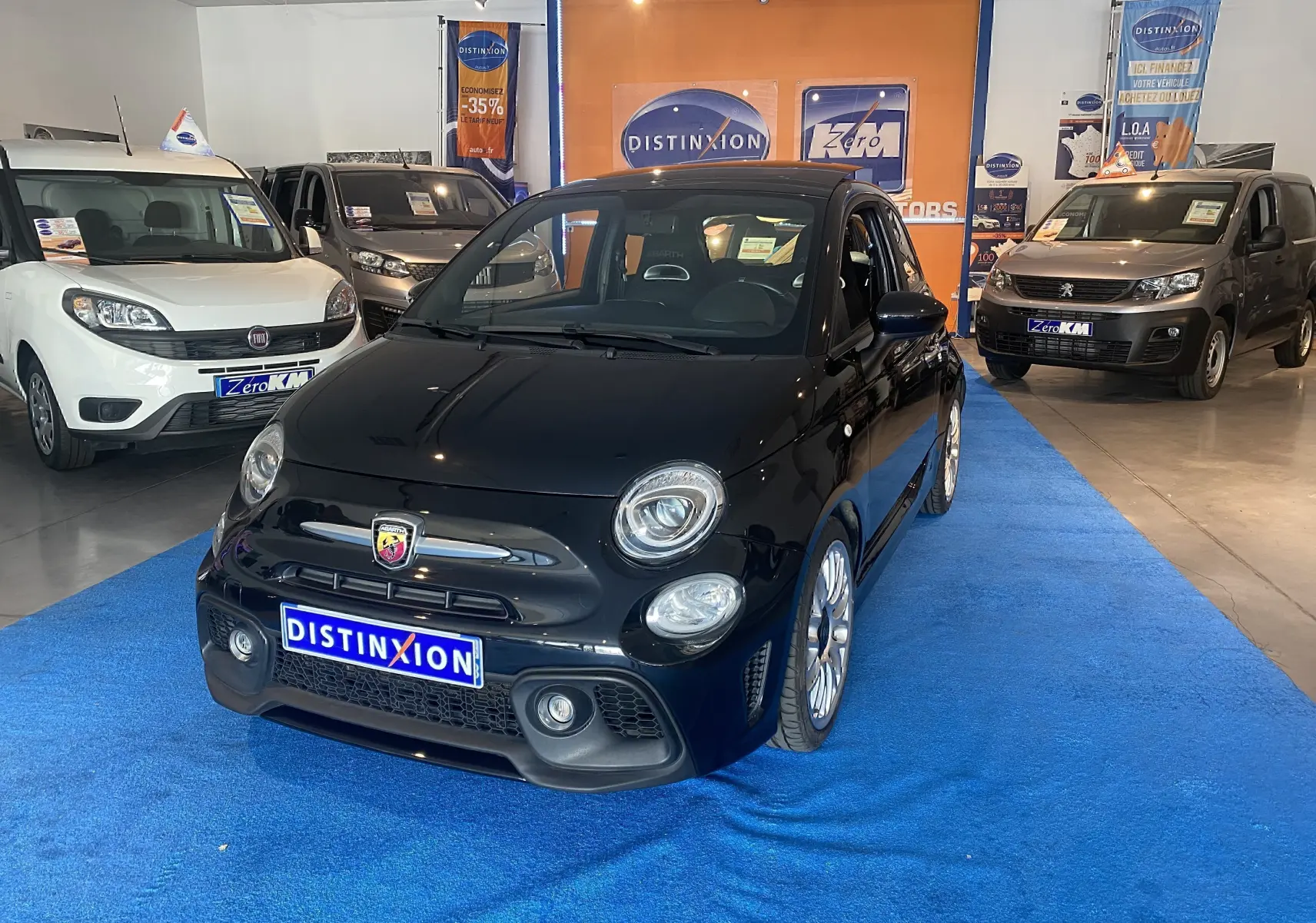 ABARTH 595 noir en 3/4 avant droit, jantes alu 17 pouces, toit ouvrant électrique, en showroom sur tapis bleu.