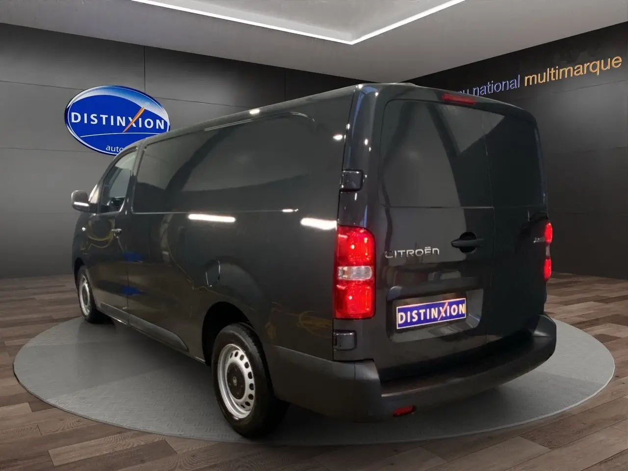 Vue 3/4 arrière droite du Citroën Jumpy Fourgon gris platinium avec feux arrière allumés en showroom.