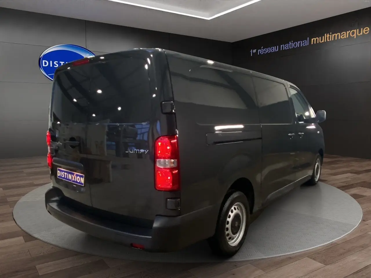 Vue 3/4 arrière droite du Citroën Jumpy Fourgon gris platinium avec feux arrière allumés en intérieur showroom.