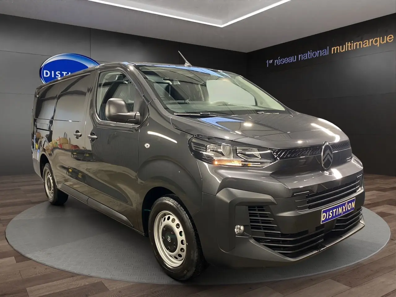 Vue 3/4 avant droit d’un Citroën Jumpy Fourgon gris platinium dans un showroom avec éclairage intérieur.