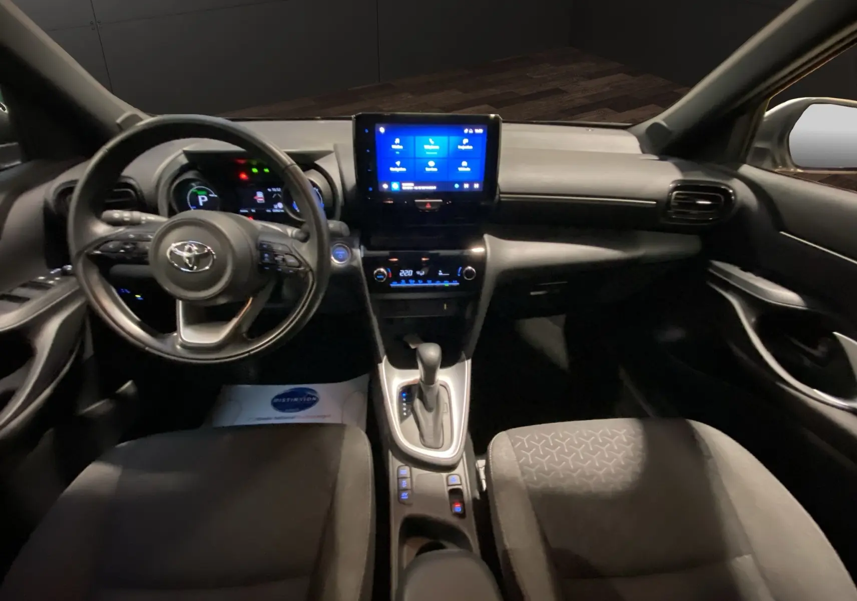 Vue intérieure avant de la Toyota Yaris Cross 116H Design 2023, tableau de bord noir avec écran tactile central lumineux.