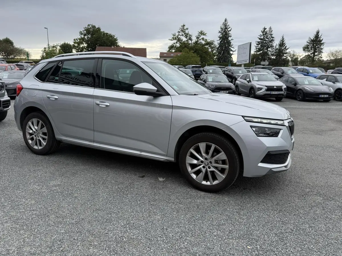 Vue profil droit d'un Skoda Kamiq gris métallisé 2022, avec jantes alliage et barres de toit argentées sur parking.