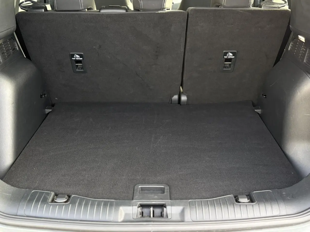 Coffre spacieux du Ford Kuga 2024 vu de face, avec plancher de coffre ajustable et sièges arrière noirs relevés.