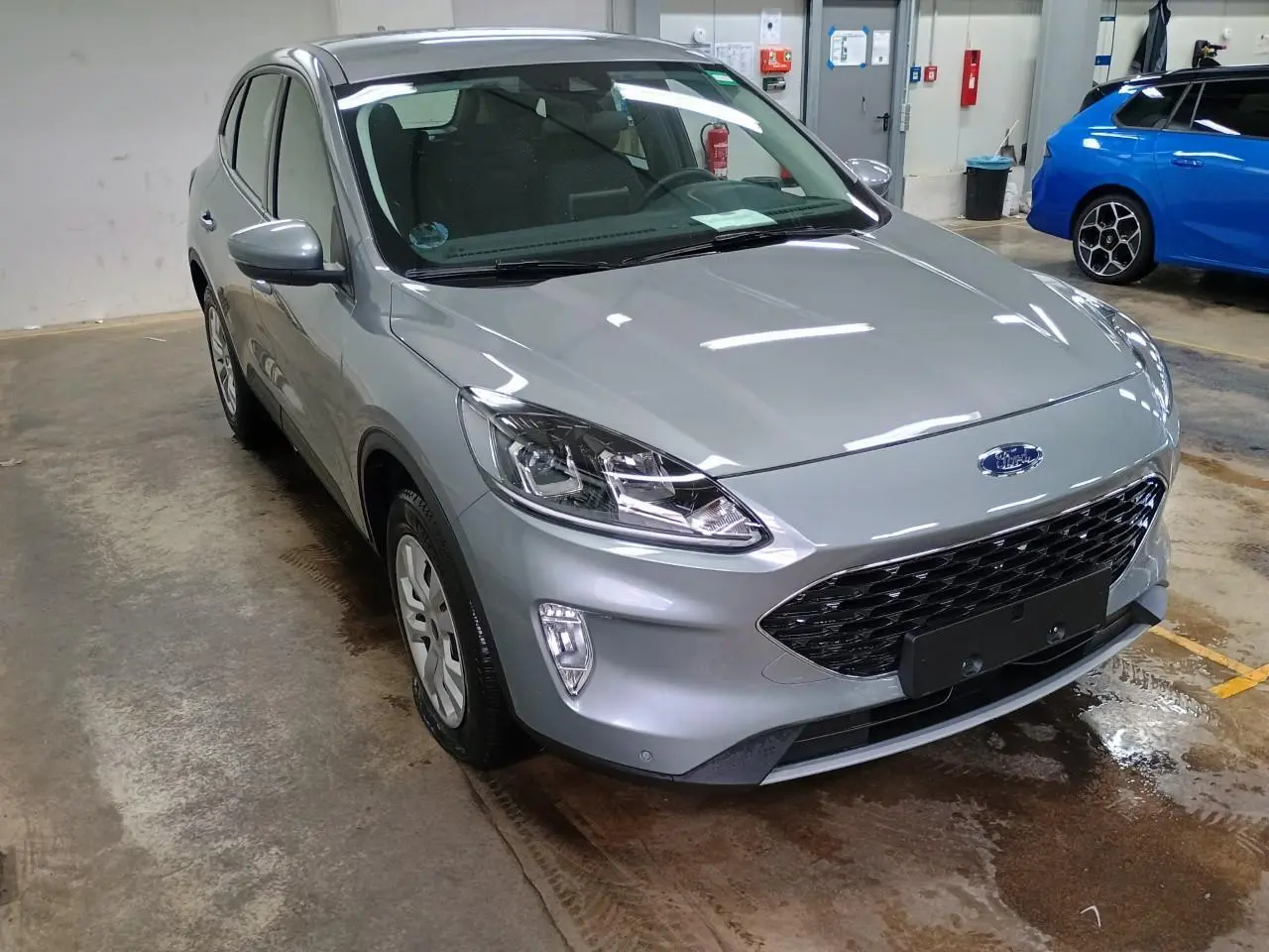 Ford Kuga gris Solar en 3/4 avant droit dans un garage, mettant en valeur sa calandre noire et ses phares LED.
