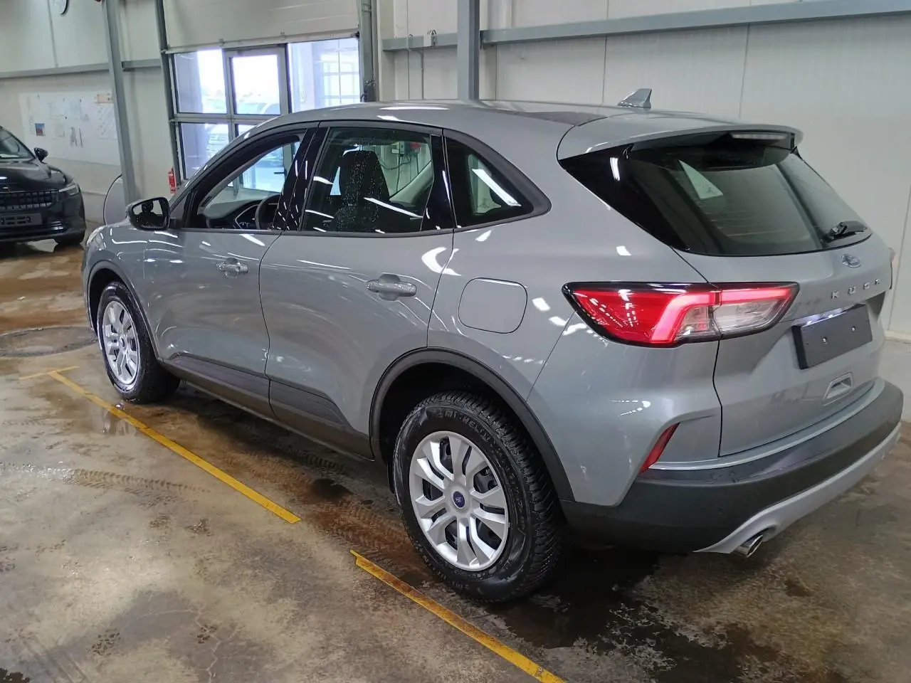 Ford Kuga gris Solar vu de 3/4 arrière droit dans un garage, avec feux arrière allumés et jantes argentées.