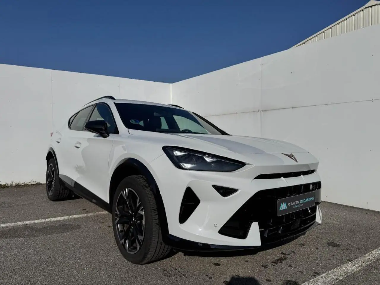 Vue 3/4 avant droit d'une CUPRA Formentor blanc nacré avec toit noir et jantes alliage noires dans un parking extérieur.