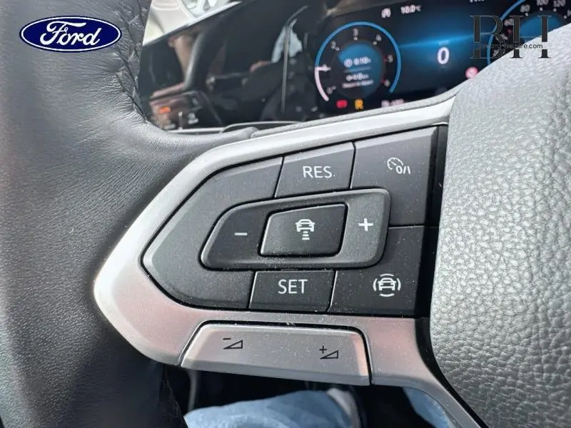 Gros plan sur les commandes au volant côté gauche d'une Volkswagen Golf gris lunaire, avec affichage numérique en arrière-plan.