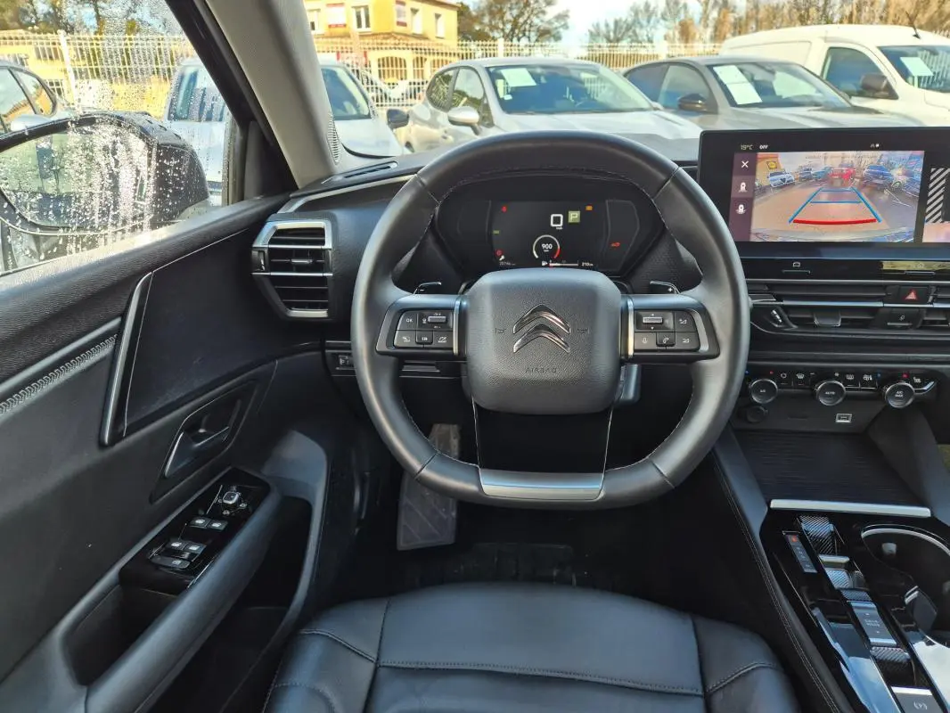 Vue intérieure centrée sur le volant cuir noir et le tableau de bord digital de la Citroën C5 X 2024 avec écran de caméra de recul.