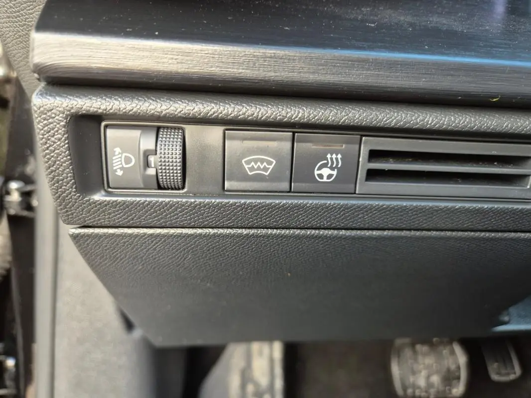 Gros plan sur les commandes noires du tableau de bord côté gauche du Citroën C5 X 2024, avec réglage des phares et chauffage du volant.