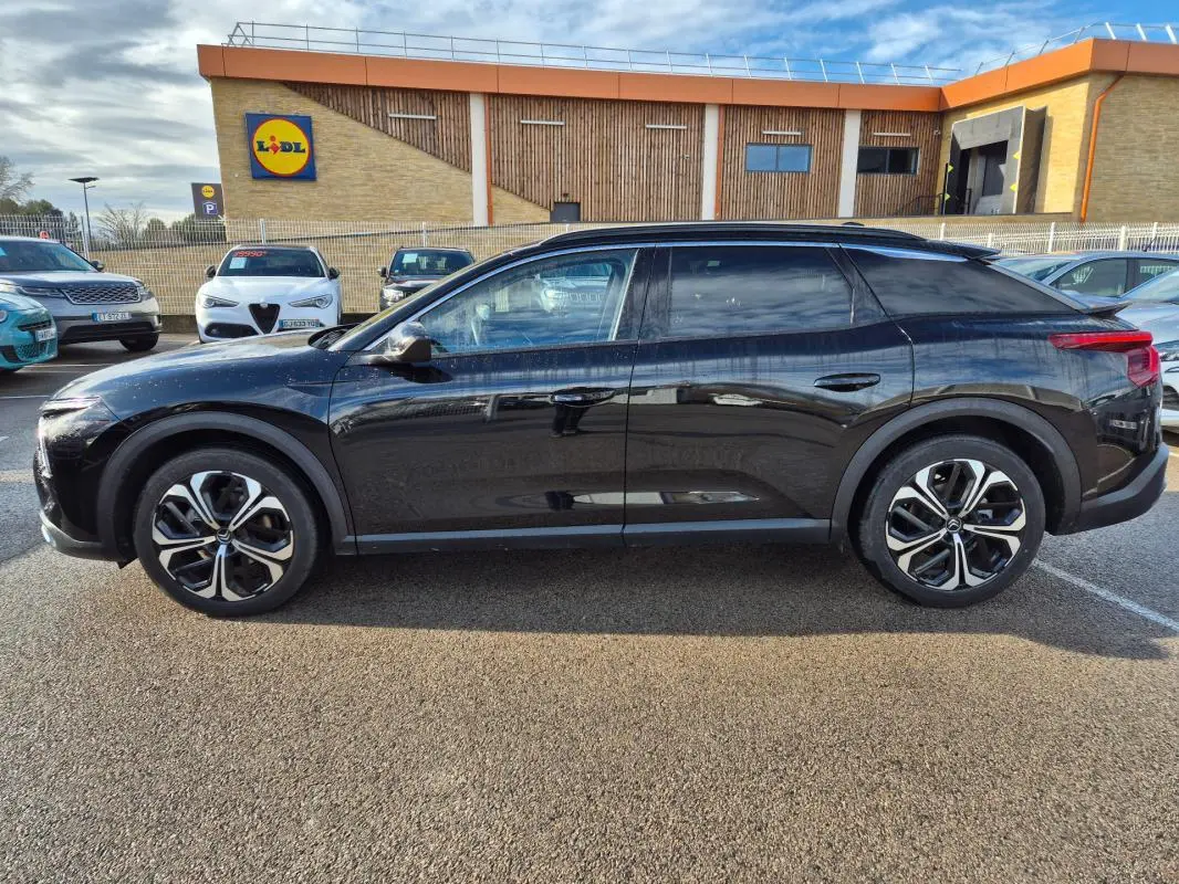 Vue de profil côté gauche d'une Citroën C5 X noire 2024 avec jantes alliage 19 pouces sur parking extérieur.