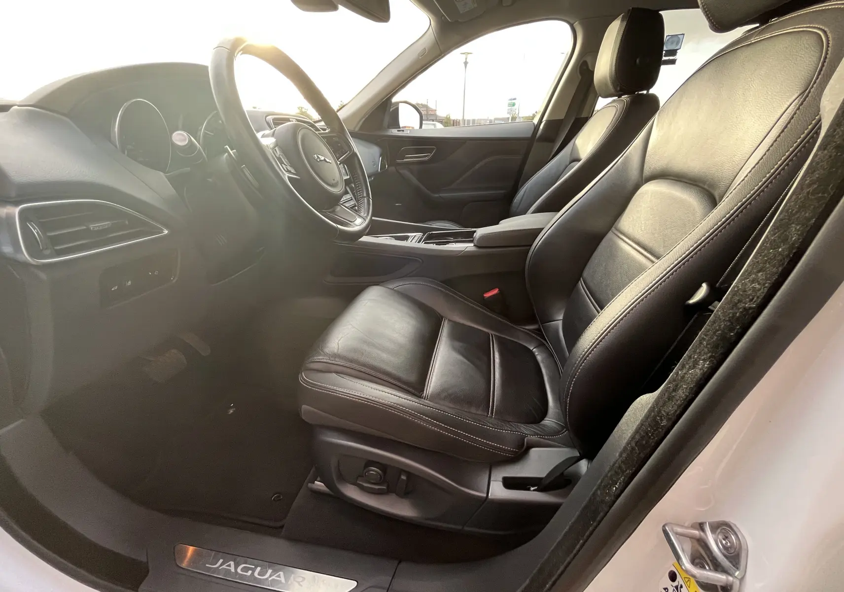 Vue intérieure côté gauche du Jaguar F-PACE blanc 2018, mettant en valeur les sièges en cuir noir et le volant multifonction.