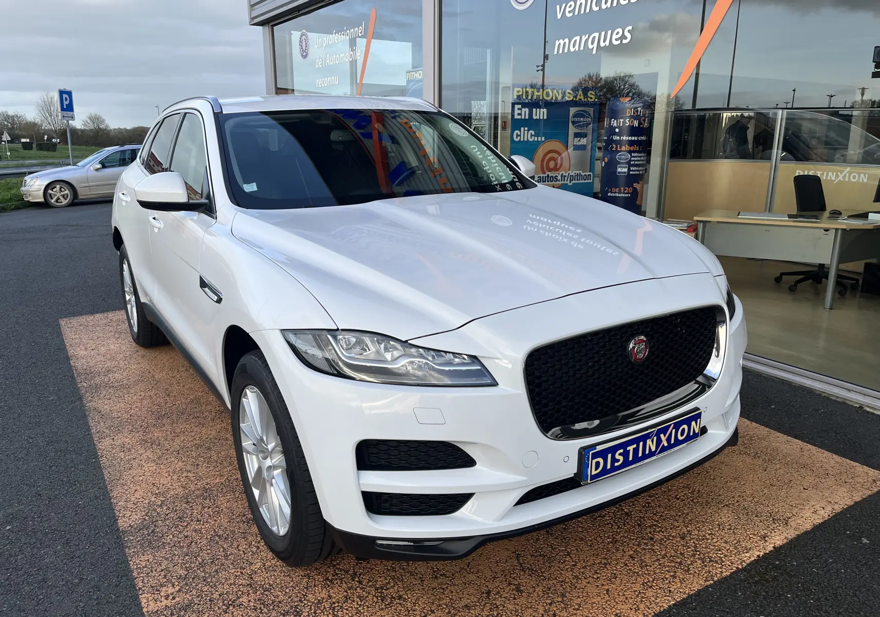 Jaguar F-PACE blanc vue 3/4 avant droit, calandre noire distinctive et jantes alliage 19 pouces visibles.