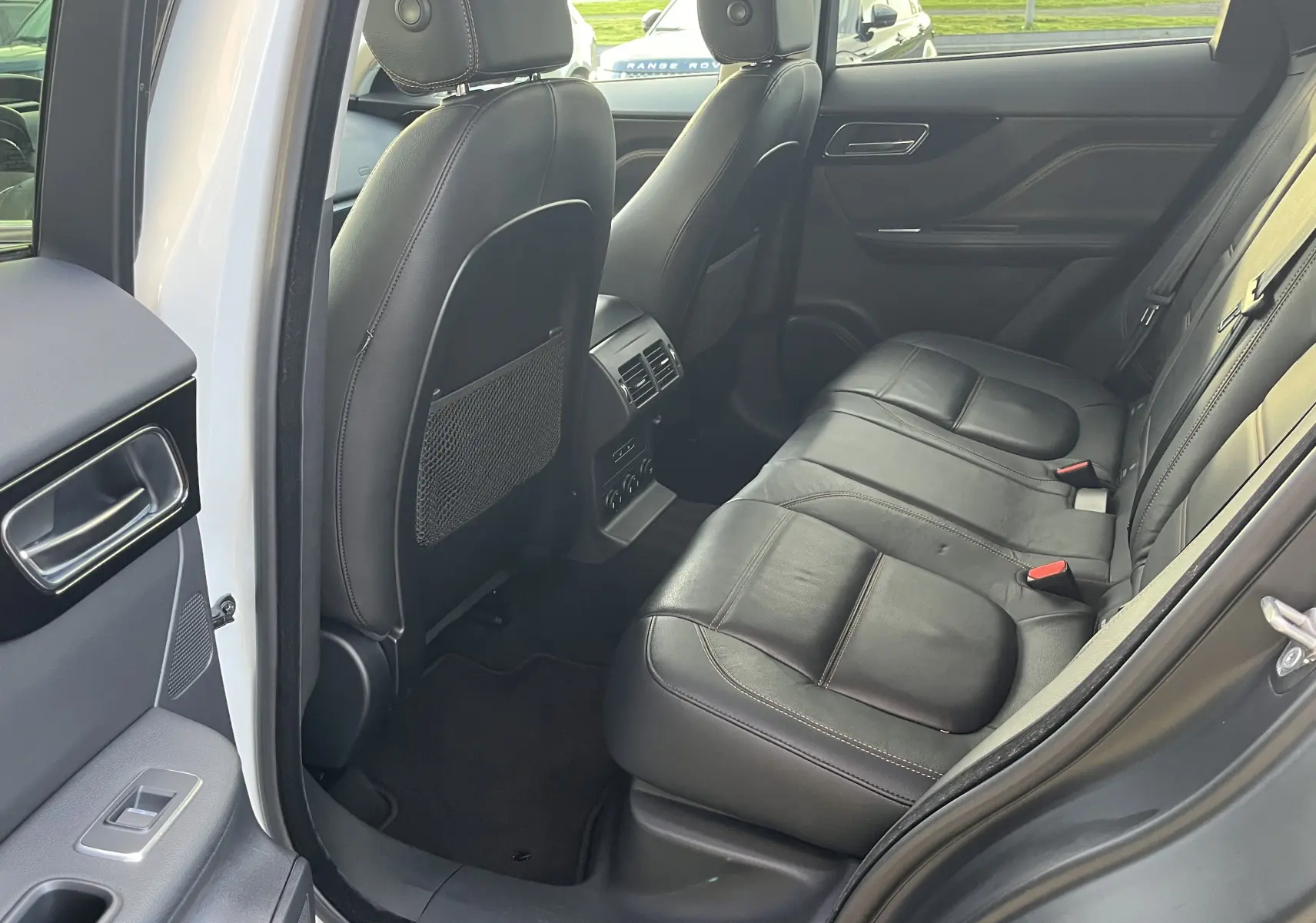 Vue intérieure côté droit des sièges arrière en cuir noir du Jaguar F-PACE blanc 2018, avec porte ouverte.