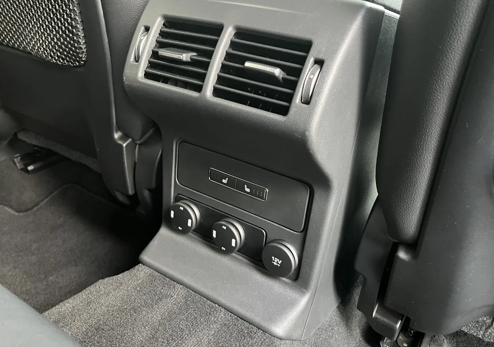 Vue rapprochée de la console arrière noire du Jaguar F-PACE 240D Prestige 2018 avec aérateurs et commandes de sièges chauffants.