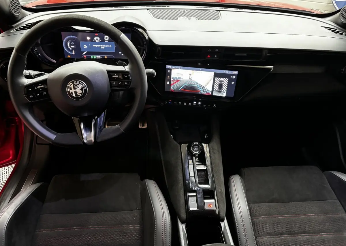 Vue intérieure avant de l'Alfa Romeo Junior 2024, volant cuir, écran tactile central affichant l'aide au stationnement.