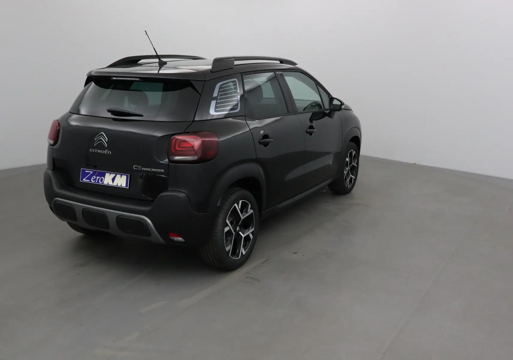 Vue 3/4 arrière droite d'un Citroën C3 Aircross noir avec jantes alliage et barres de toit visibles.