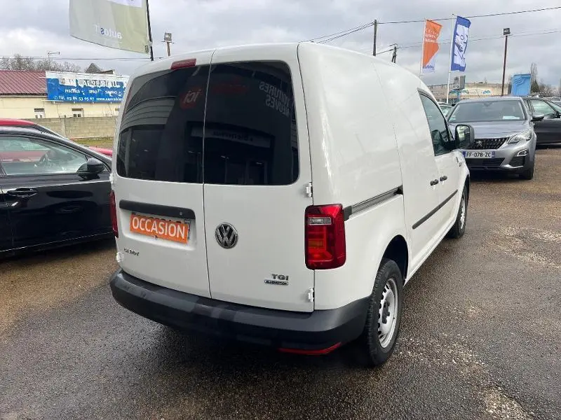 Vue 3/4 arrière droite d'un Volkswagen Caddy Van blanc Candy avec portes arrière vitrées teintées et logo TGI GNV visible