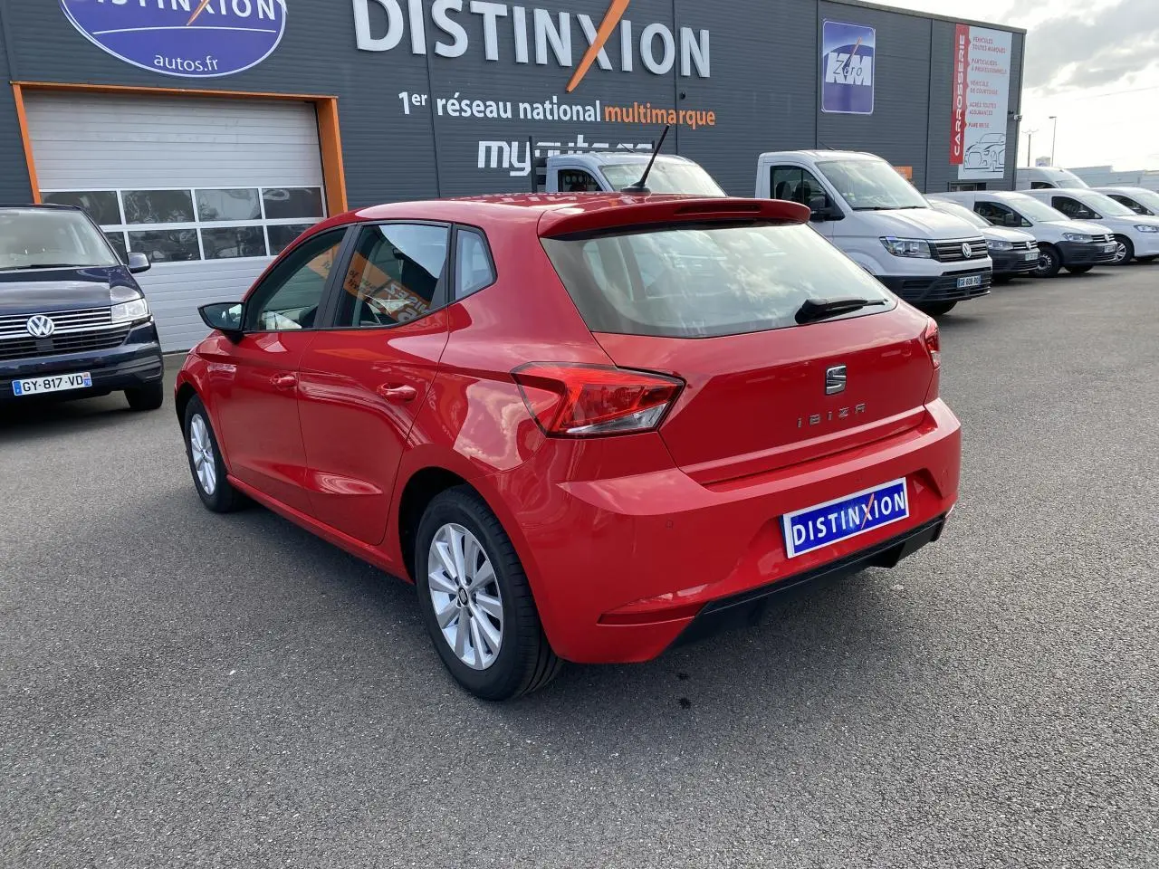 Vue 3/4 arrière gauche d'une SEAT Ibiza rouge pur 2021 avec jantes alliage 15 pouces, stationnée devant un concessionnaire multimarque.
