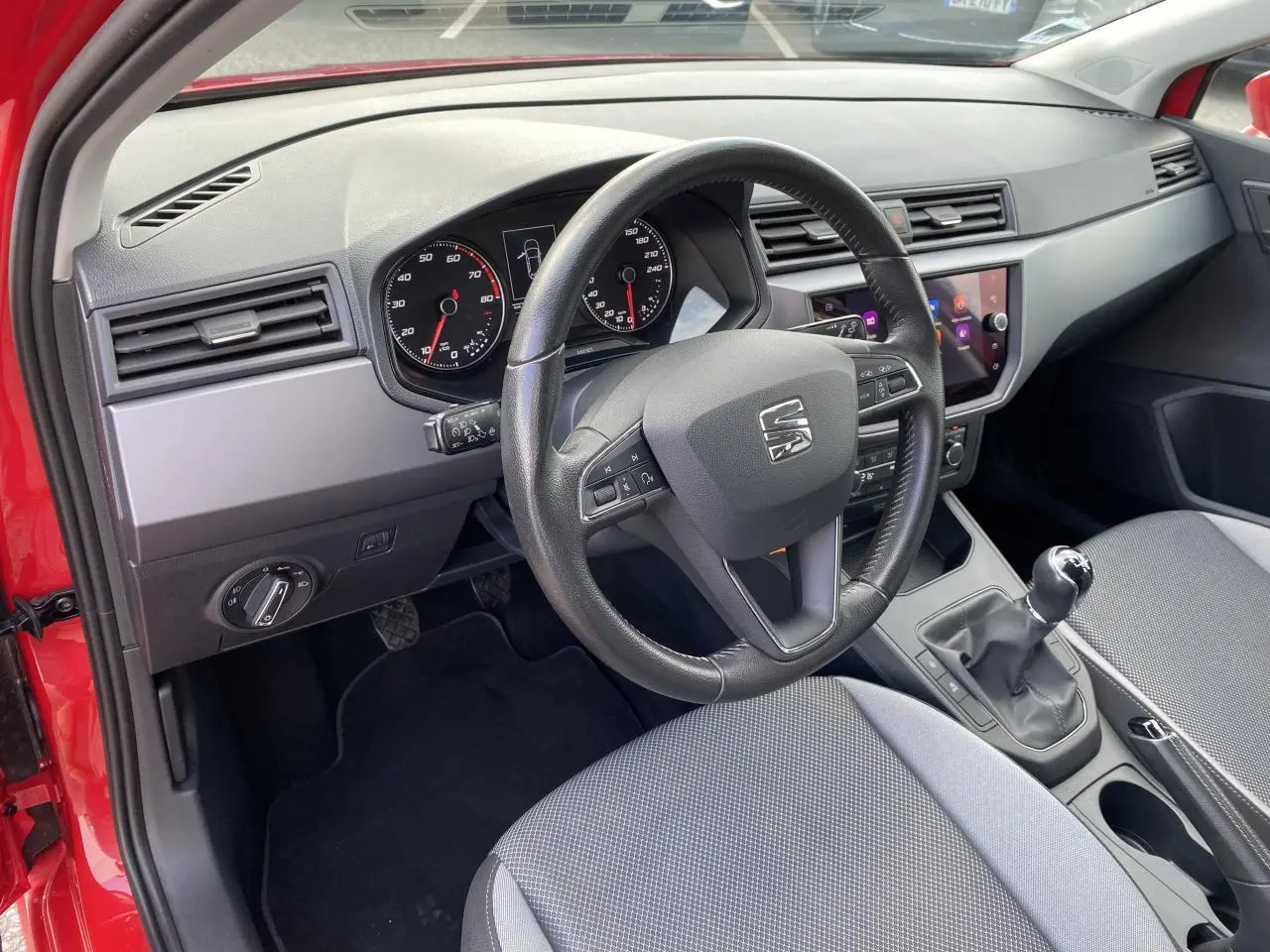 Vue intérieure côté conducteur d'une SEAT IBIZA rouge pur 2021, volant cuir multifonctions et boîte manuelle visibles.