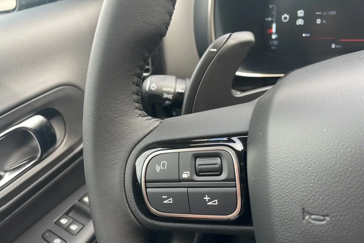 Gros plan sur les commandes au volant du Citroën C5 Aircross Hybrid 2025, intérieur noir avec détails chromés.