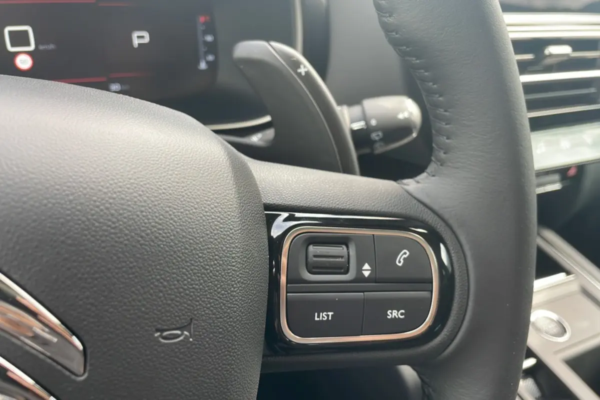 Gros plan sur les commandes du volant cuir noir du Citroën C5 Aircross Hybrid 2025, affichage numérique en arrière-plan.