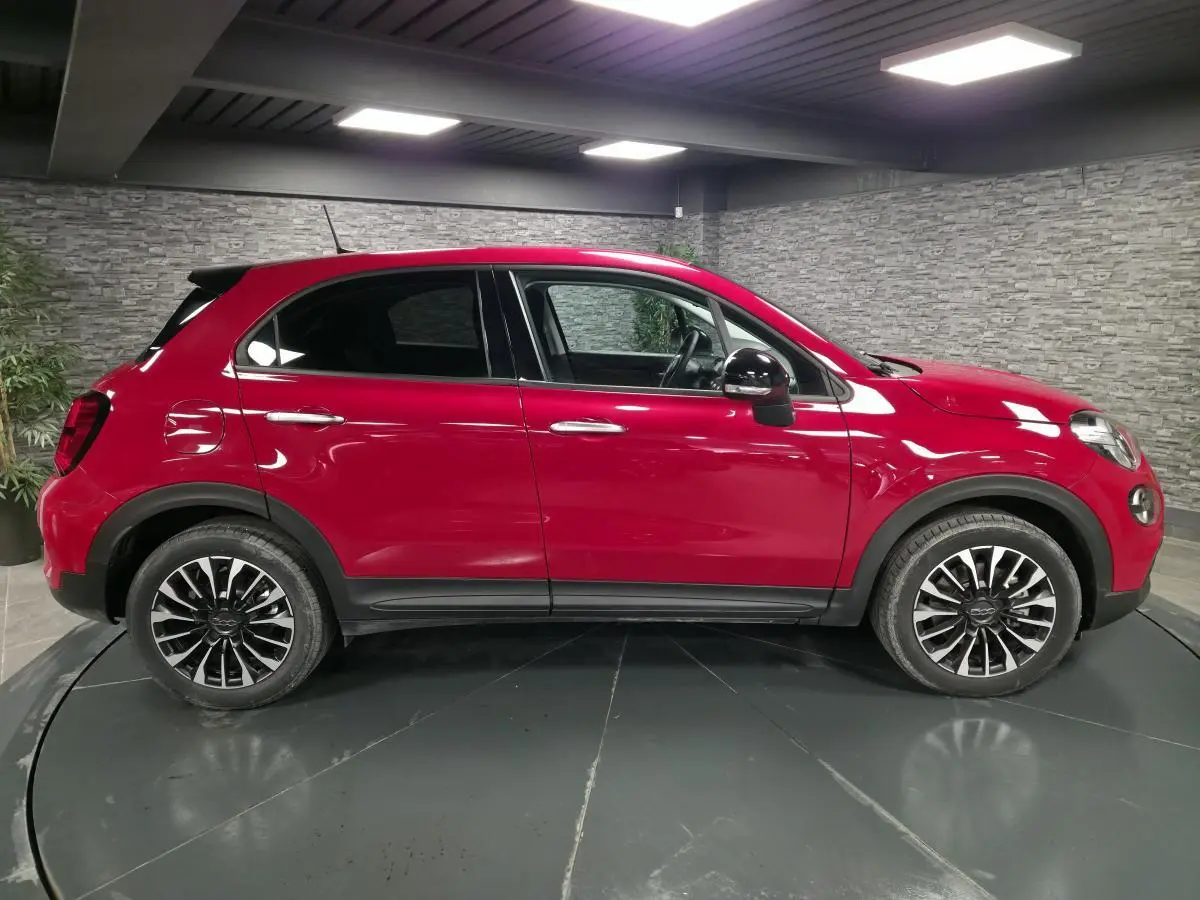 Vue latérale droite d'un Fiat 500X rouge avec jantes alliage noires et vitres surteintées dans un showroom.