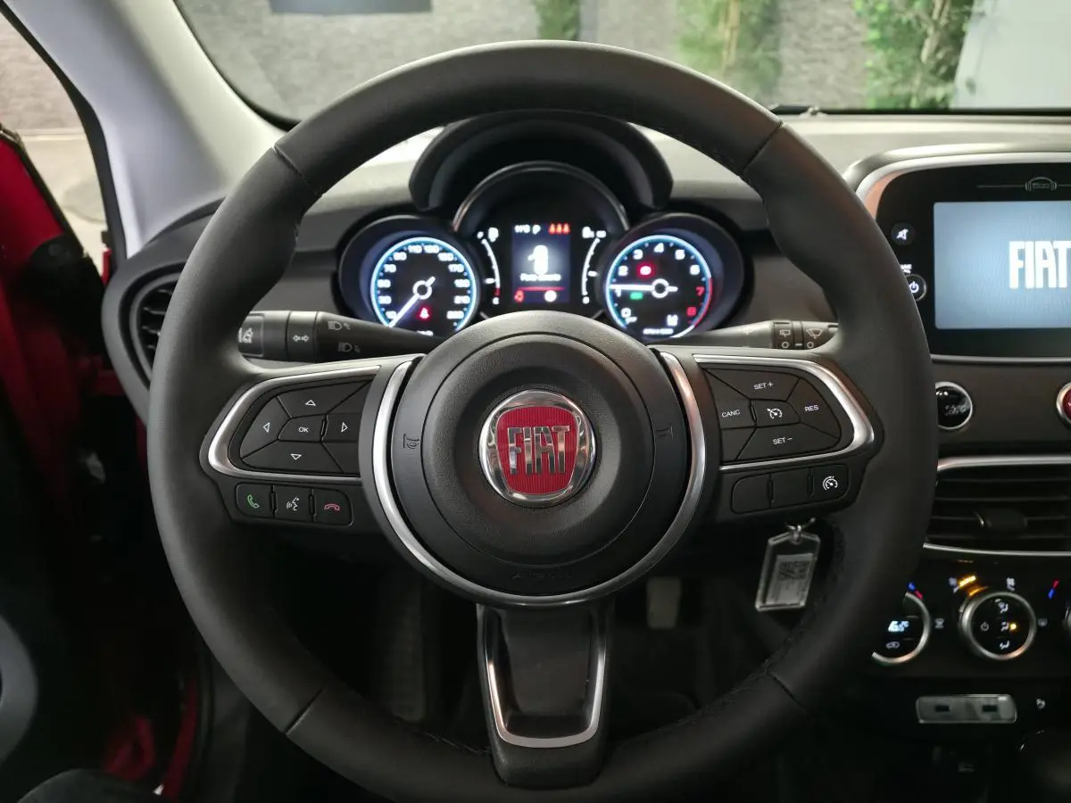 Vue centrée sur le volant noir du Fiat 500X 2024 avec tableau de bord et écran multimédia allumé.