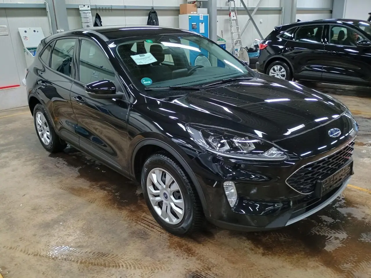 Ford Kuga noir Obsidien vu en 3/4 avant droit dans un garage, mettant en valeur sa calandre et ses phares modernes.