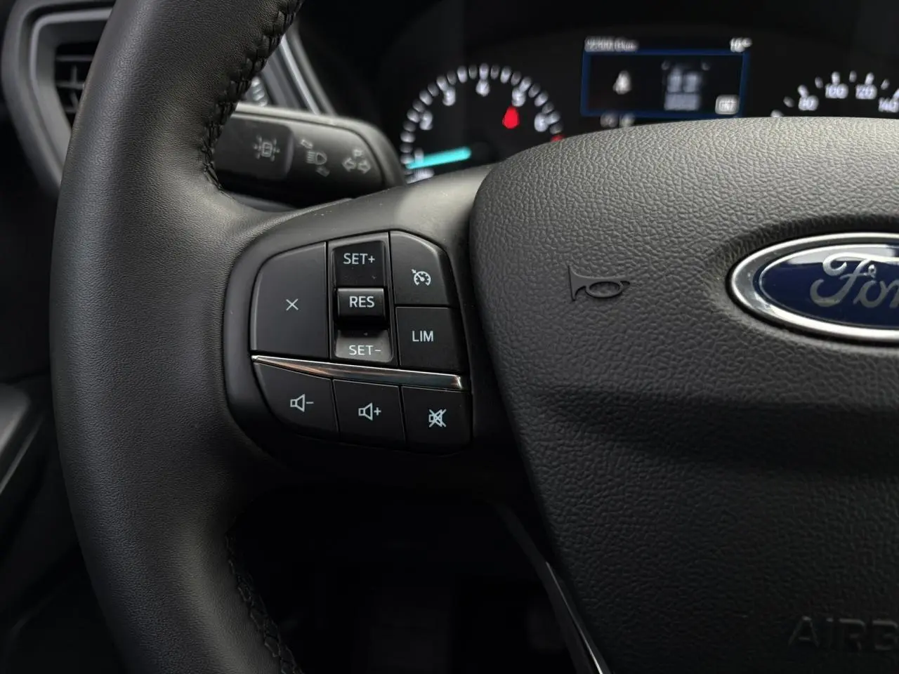 Gros plan sur le volant en cuir noir du Ford Kuga 2024, avec commandes multifonctions et logo Ford visible.