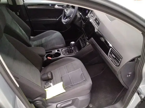 Vue intérieure côté conducteur du Volkswagen Touran gris 2025, avec tableau de bord noir brillant et sièges tissu foncé.