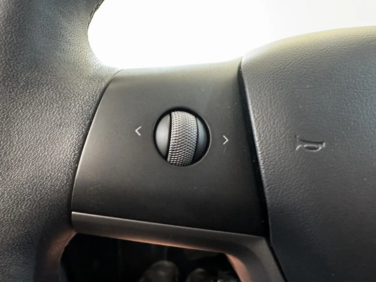 Gros plan sur la molette de réglage multifonctions du volant en cuir noir d'une Tesla Model 3 Grande Autonomie 2023.