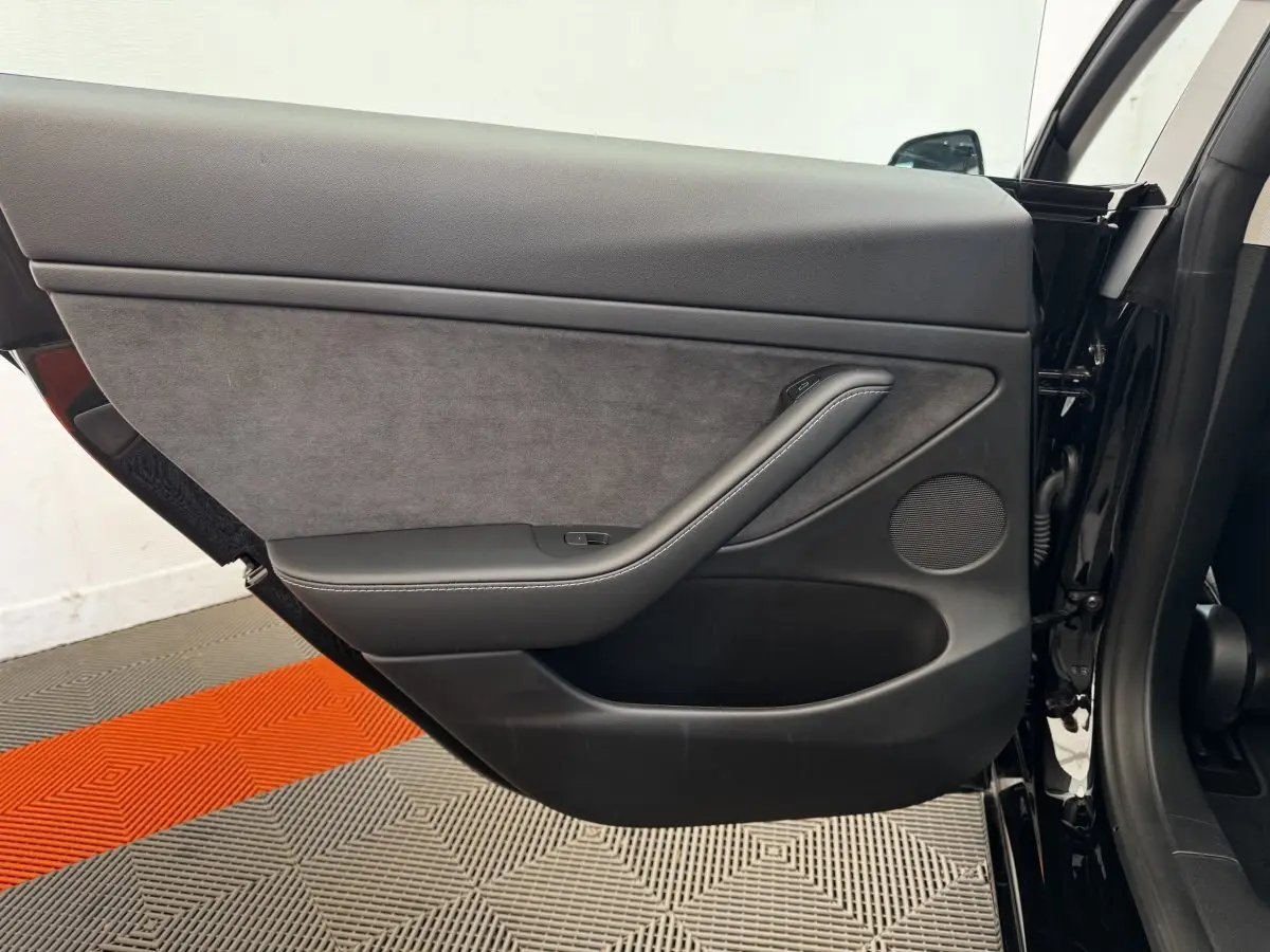 Vue côté intérieur de la porte arrière gauche noire d'une Tesla Model 3 2023 avec garniture tissu et cuir.