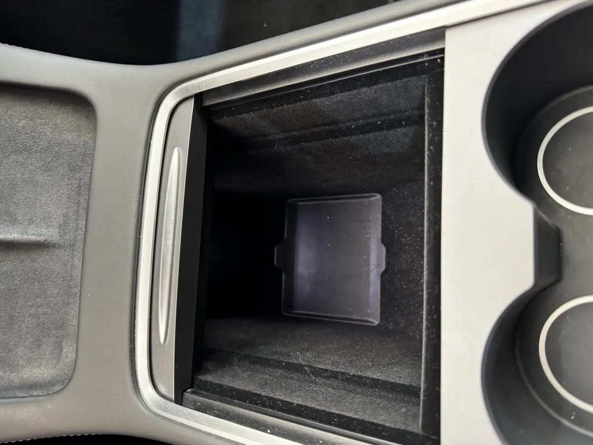 Vue rapprochée de la console centrale noire de la Tesla Model 3 2023, avec compartiment de rangement ouvert et porte-gobelets.