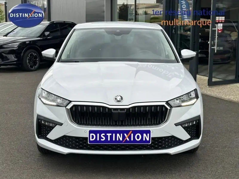 Vue frontale d'une Skoda Scala blanc cristal avec calandre chromée et feux LED, stationnée devant un showroom.