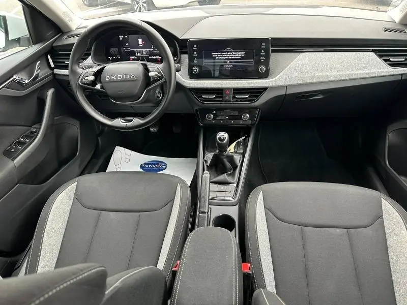 Vue intérieure avant de la Skoda Scala 2025 avec tableau de bord moderne, volant cuir multifonction et sièges tissu noir/gris.