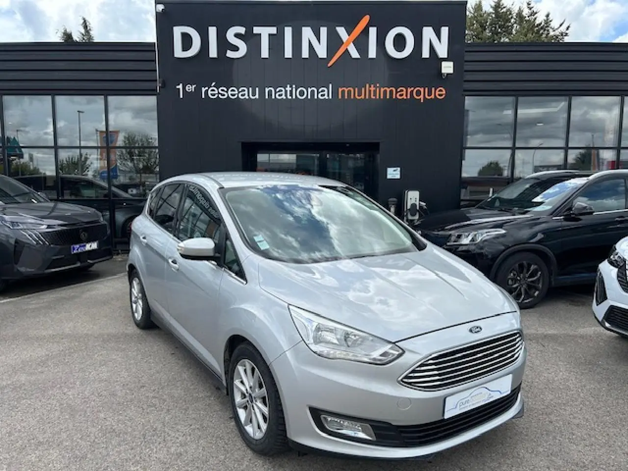 Ford C-MAX II gris clair métal en 3/4 avant droit, avec calandre chromée et jantes alliage 16 pouces visibles.