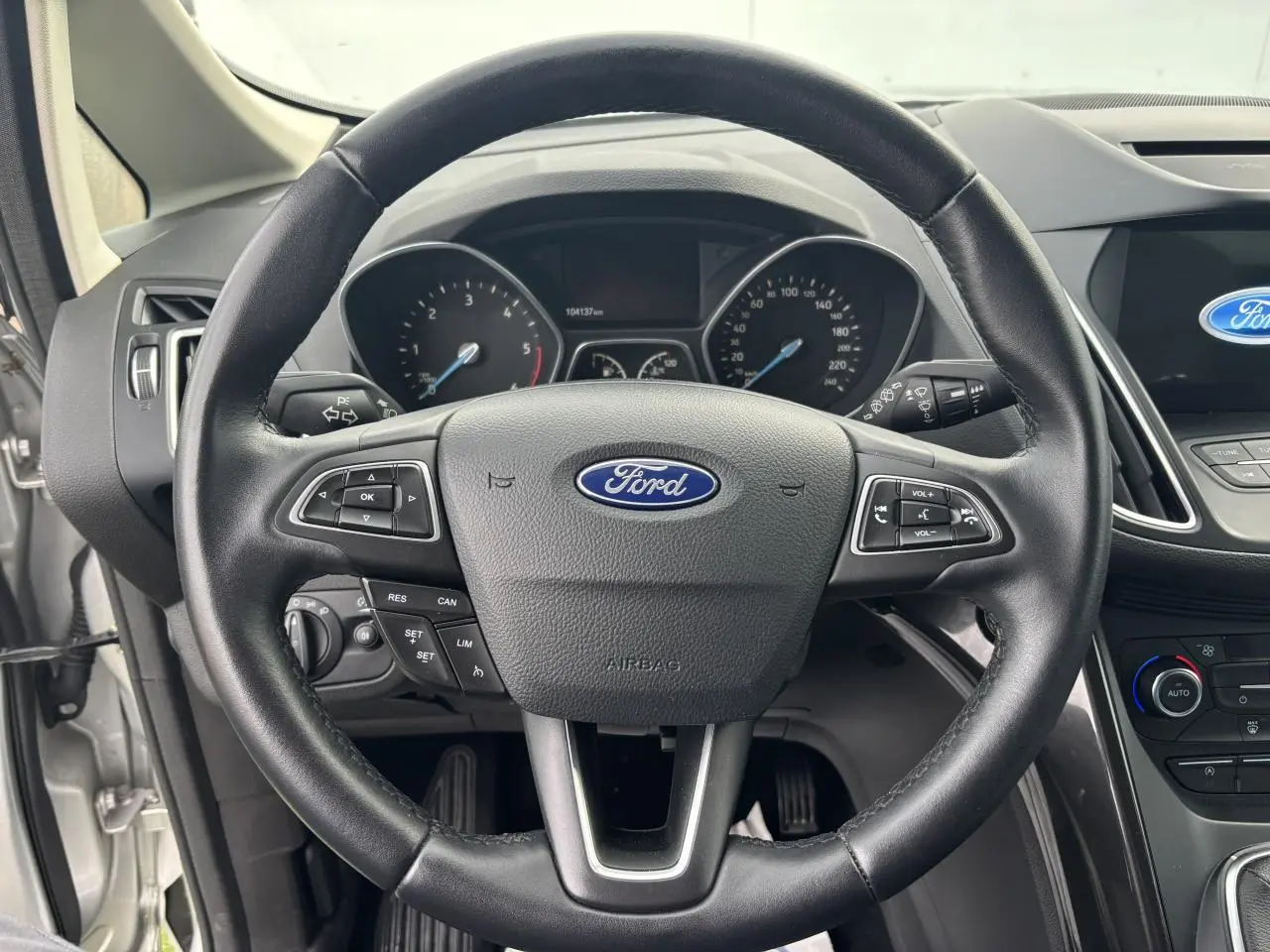 Vue rapprochée du volant cuir noir de la Ford C-MAX II avec tableau de bord et écran tactile visible à droite.